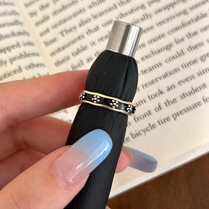 Detailed macro view of black enamel ring featuring golden floral patterns on a finger