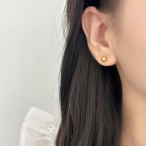Close-up of minimalist gold ball stud earrings worn by a model with a polished finish