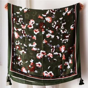 Detail of dark green floral cotton scarf with tassels and red-striped borders