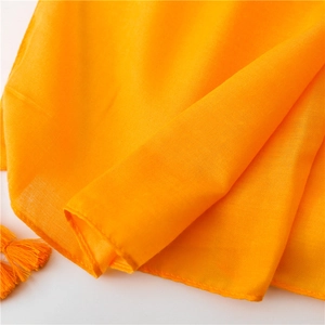 Close-up of bright orange cotton linen scarf fabric showing texture and tassel details