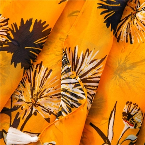 Dettaglio della sciarpa in cotone giallo con stampa floreale e nappe decorative bianche