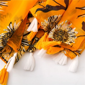 Dettaglio di una sciarpa in cotone giallo con stampa girasole e nappine a frangia bicolore