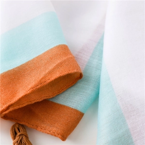 Détail de l'écharpe légère en coton et lin avec rayures colorées et pompons orange
