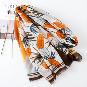 Detail of tropical leaf print scarf with raw fringe edges on minimalist white tabletop