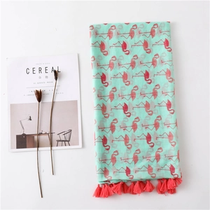 Detailed flat lay of mint green scarf with flamingo print and red fringe tassels