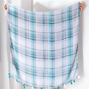 Macro detail of plaid scarf fabric featuring turquoise checkers and fine fringed edges