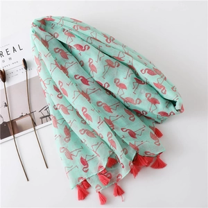 Close-up of mint green scarf with red flamingo print and fringe on a white surface