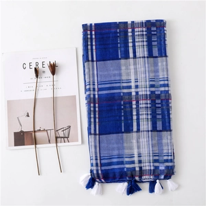 Detail of blue and white plaid scarf with decorative pom-pom tassels and soft texture