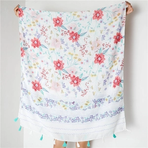 Détail de l'imprimé floral rouge et des pompons turquoise sur une écharpe blanche