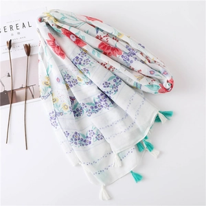 Détail d'une écharpe bohème blanche à imprimé fleuri et bords à pompons turquoise