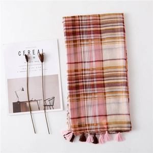 Macro shot of plaid scarf fringe detail with pink and brown tassels on white surface