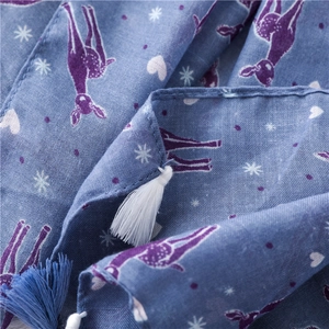 Detailed close-up of blue scarf fabric with purple deer print and handmade fringe tassels