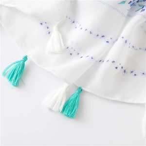 Vue macro d'une écharpe bohème blanche à motifs floraux avec détails de pompons