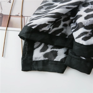 Detailed close-up of leopard print scarf featuring black stitched edges and soft fabric