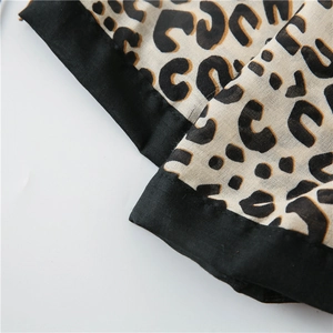 Detail of leopard print scarf with black border trim and fine stitching on cotton linen
