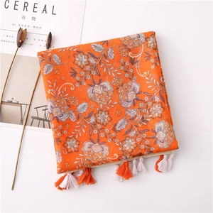 Detailed view of vibrant orange floral scarf with intricate blue and white patterns and tassels
