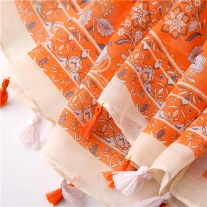Detailed macro view of bohemian scarf fabric with orange floral patterns and colorful tassels
