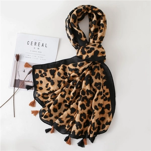 Detail of leopard print scarf with soft tassels and elegant lifestyle props on white surface