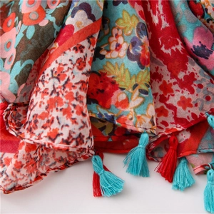 Detailopname van een bohemien bloemenprint sjaal met rood-blauwe kwastjes aan de rand
