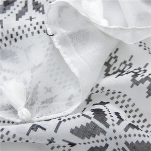 Close-up of white cotton linen scarf featuring black geometric patterns and fringe tassels