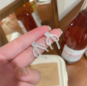 Close-up of silver bow earrings with heart-shaped zircon and lace-textured hollow design