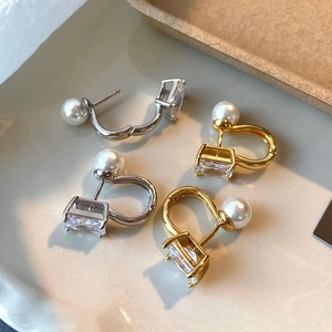 Square zircon and pearl drop earrings in silver and gold displayed on a ceramic tray