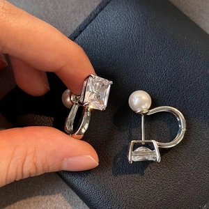 Detail of U-shaped silver earrings with square zircon and premium white pearl on leather
