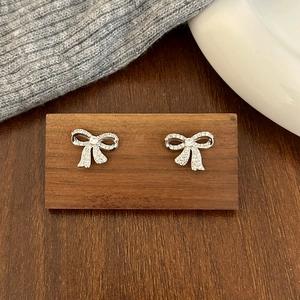 Close-up of silver bow stud earrings with sparkling pavé zircons on a wooden display