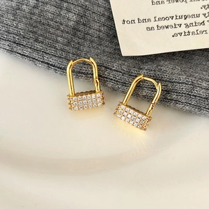 Detailed close-up of golden padlock earrings with pavé cubic zirconia on a white surface