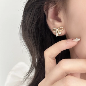 Elegant gold bow earrings with sparkling white cubic zirconia shown on model ear