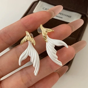 Elegant gold and white fishtail stud earrings shown held by hand against a jewelry box