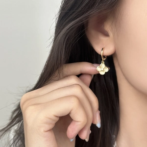 Elegant gold clover drop earrings with white stone inlay worn by a model in a side view