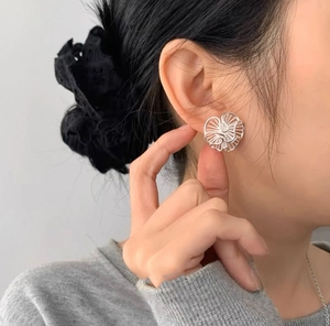 Detailed close-up of hollowed-out silver flower stud earrings worn on earlobe