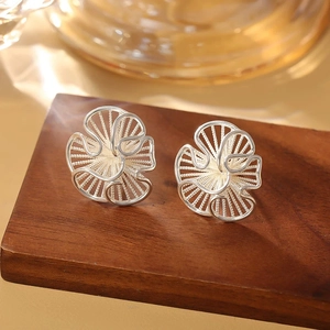 Macro detail of silver floral stud earring with intricate hollow wirework on wood stand