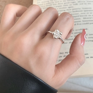 Minimalist silver flower ring with zircon inlay shown on finger over an open book