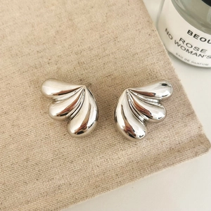 Macro detail of silver wing-shaped stud earrings on rustic linen with a candle background