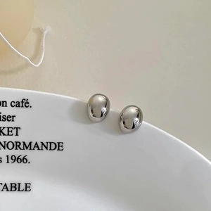 Close-up of polished silver oval stud earrings resting on a decorative ceramic saucer