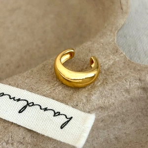 Detailed view of a polished gold C-shaped ear cuff on a textured handmade background