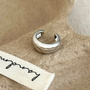 Detailed macro view of a silver-polished C-shaped ear cuff on a textured background
