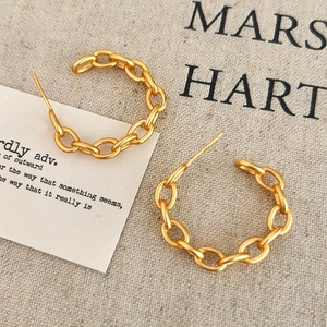 Detailed view of gold Cuban chain C-shape stud earrings on a textured fabric background