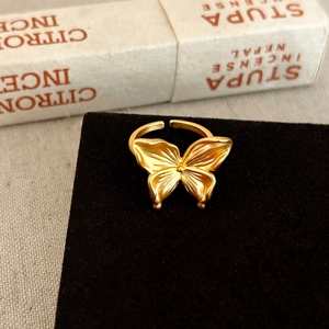 Détail d'une bague papillon en or mat avec texture d'aile délicate sur support