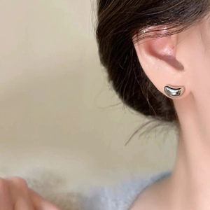 Minimalist silver bean stud earrings with polished finish on model's ear for daily wear