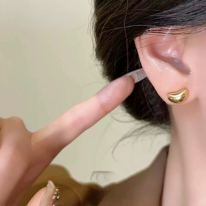 Minimalist gold bean stud earrings with a polished mirror finish on model ear