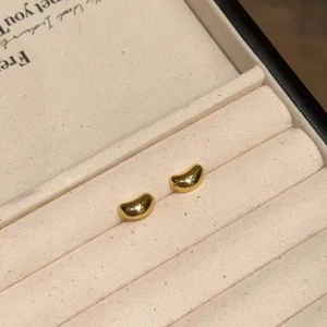 Macro detail of polished gold bean-shaped stud earrings in a beige velvet jewelry box