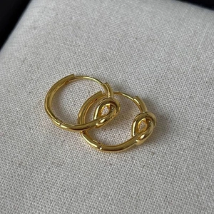 Gros plan de boucles d'oreilles nœuds dorées polies sur un tissu gris clair texturé