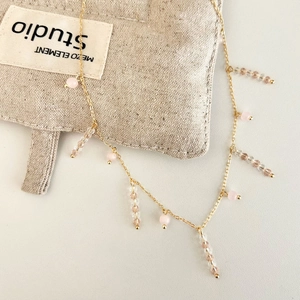 Gros plan du collier en chaîne dorée avec perles roses et pompon en perles champagne