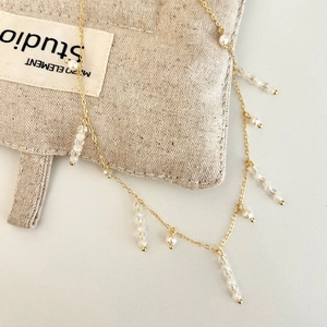 Détail d'un collier à pompon doré avec perles et perles facettées sur du lin