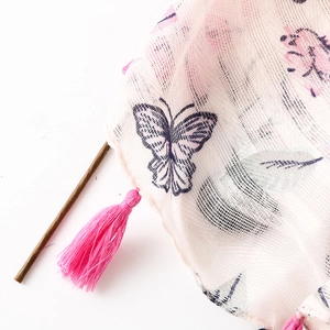 Macro shot of pink floral and butterfly print mesh fabric with decorative fringe tassels