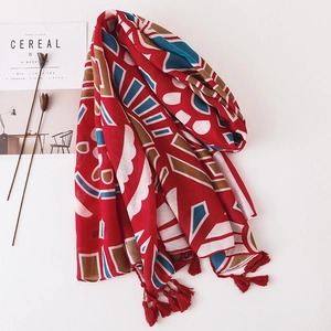 Détail d'une écharpe rouge en coton et lin avec motif géométrique et pompons à franges doux