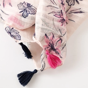 Detail of pink cotton scarf with floral print and decorative tassels on the fabric edge